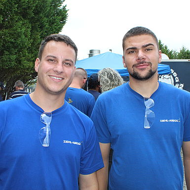 Two men with ZIEHL-ABEGG shirts smiling at the camera, safety goggles hanging on their shirt