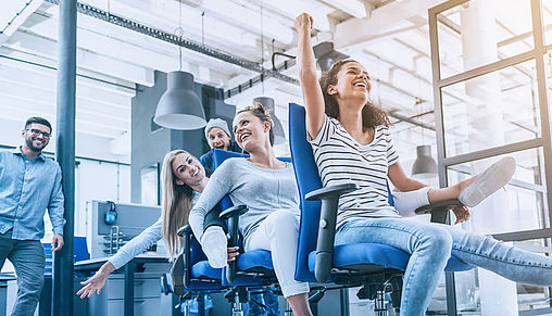 Teamgeist - Fanspirit Frauen sitzen hintereinander auf Bürostühlen & halten das Bein der hinteren