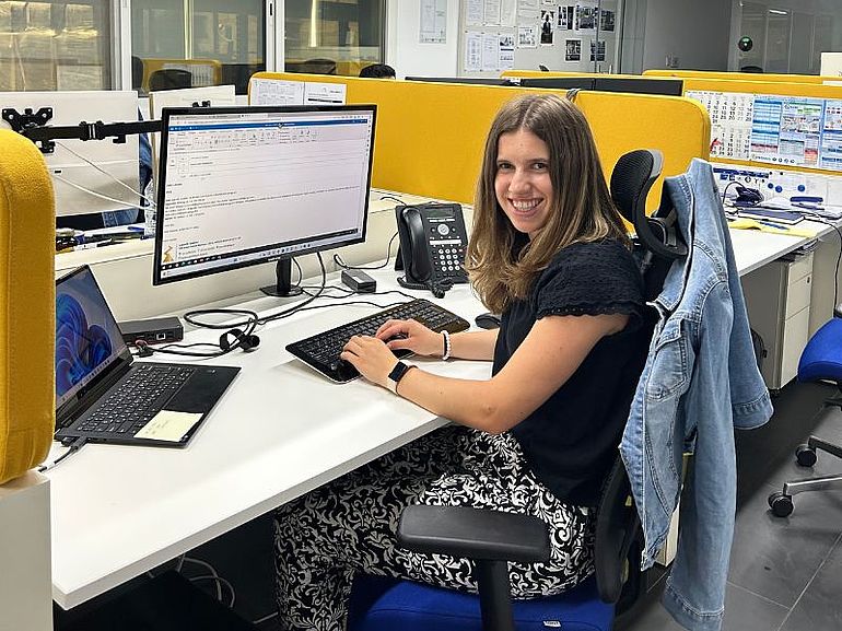 A woman at a desk in front of a computer in Dubai, turning to the camera and smiling