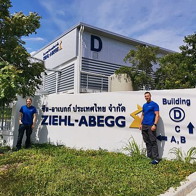 Two men standing in front of the branch in Thailand, a big logo of ZIEHL-ABEGG in two languages between them